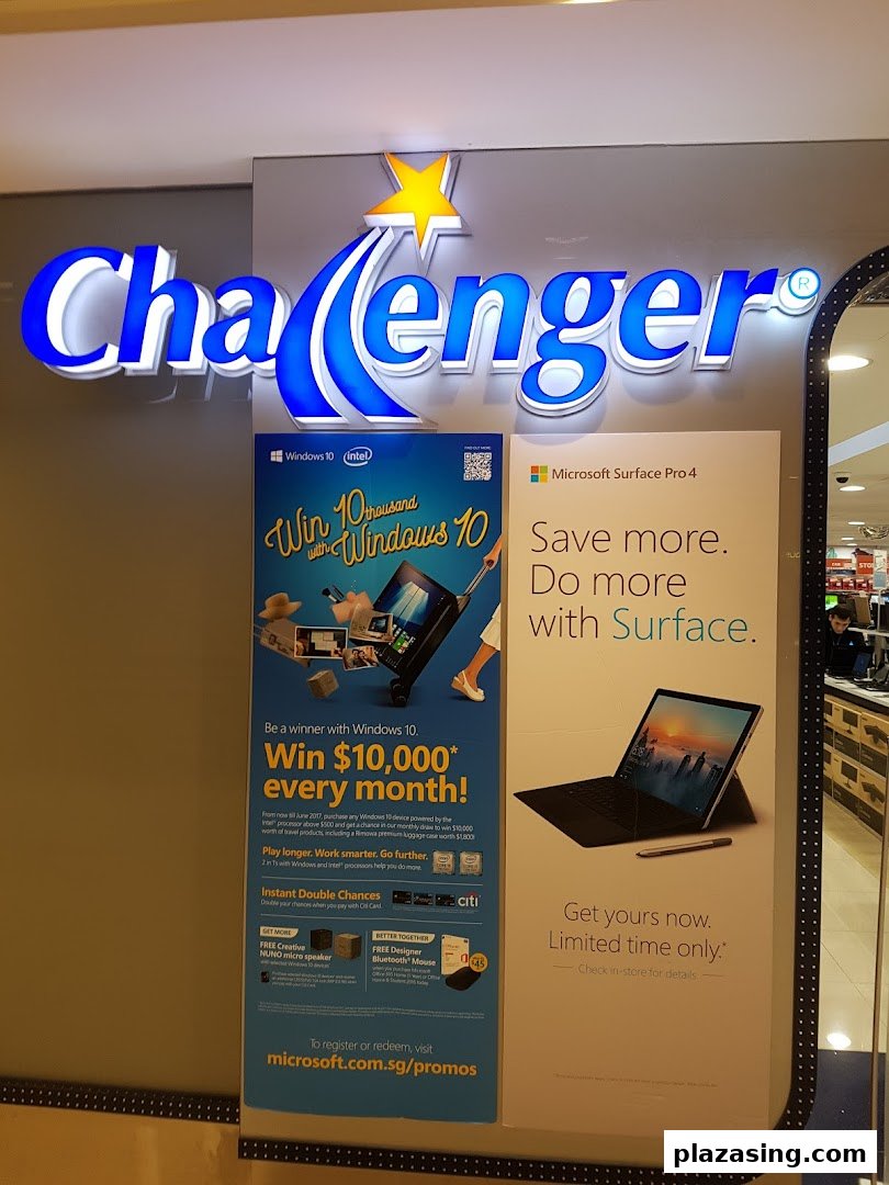 Challenger electronics store front with illuminated logo and promotional posters for Windows 10 and Microsoft Surface.