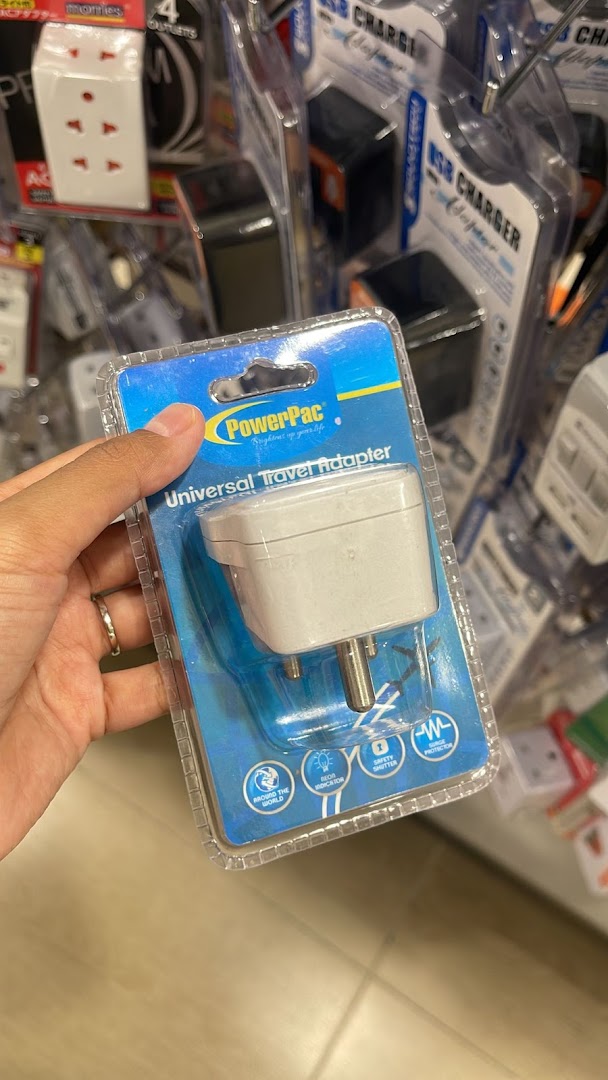 A hand holds a PowerPac universal travel adapter in its packaging, surrounded by other electronic accessories.
