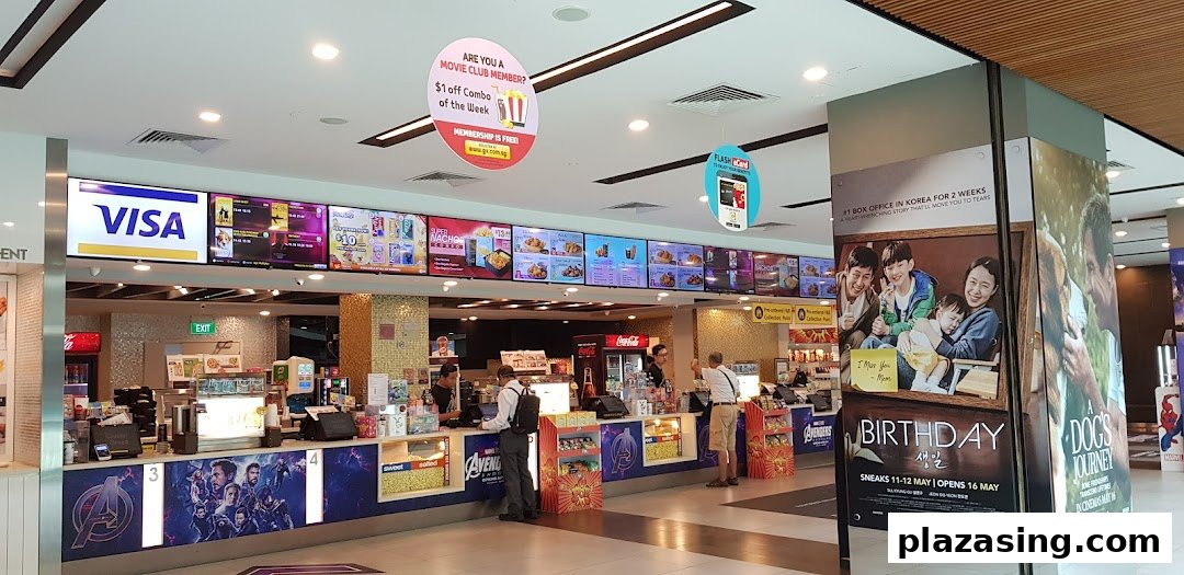 A bustling cinema concession stand with digital menu boards, offering snacks and drinks to moviegoers.
