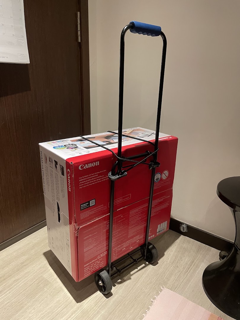 A Canon PIXMA G3020 printer box secured on a black hand trolley, likely after purchase.