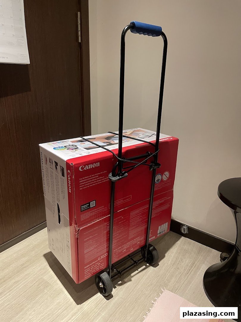A Canon PIXMA G3020 printer box secured on a black hand trolley, likely after purchase.