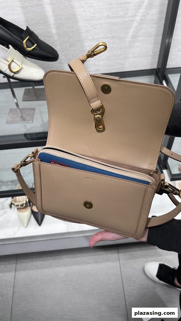 A person holds an open beige handbag, showcasing its interior and design, with shoes in the background.