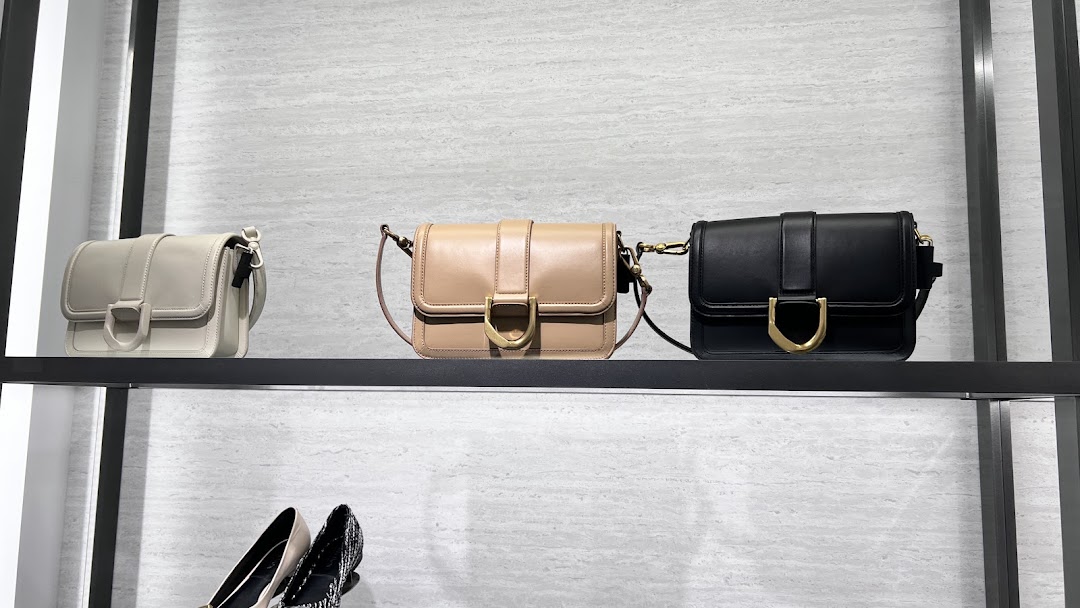 Three stylish handbags in light grey, beige, and black displayed on a retail shelf.