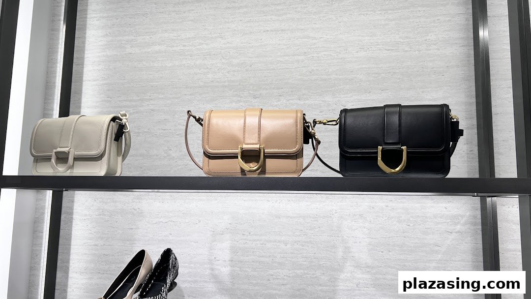 Three stylish handbags in light grey, beige, and black displayed on a retail shelf.