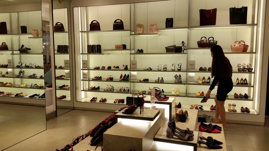 Interior of CHARLES & KEITH store displaying shoes and handbags on illuminated shelves, with a customer browsing.