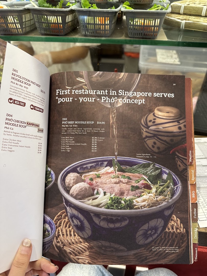 A person holds open a menu displaying various Vietnamese pho noodle soup dishes and add-ons.