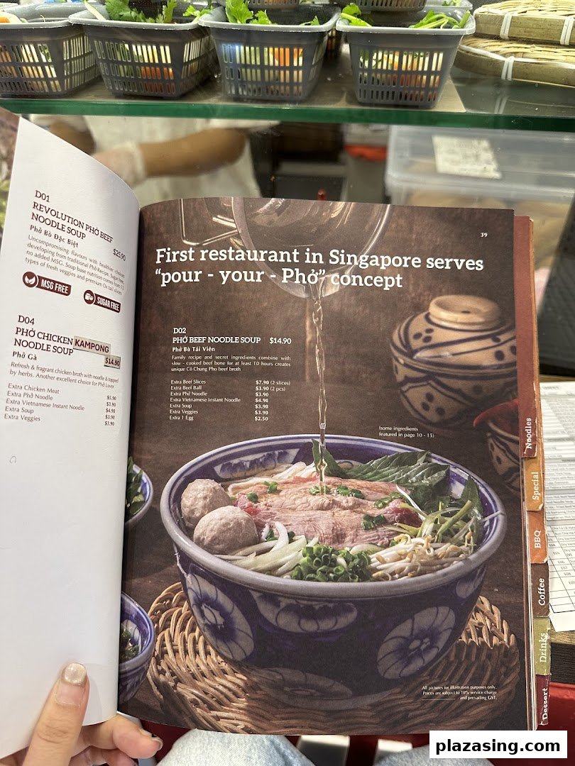 A person holds open a menu displaying various Vietnamese pho noodle soup dishes and add-ons.