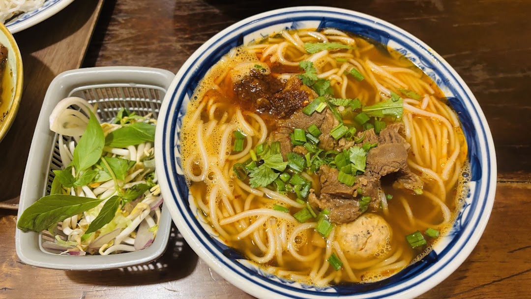 A vibrant bowl of Vietnamese noodle soup with beef, meatballs, and fresh herbs on a wooden table.