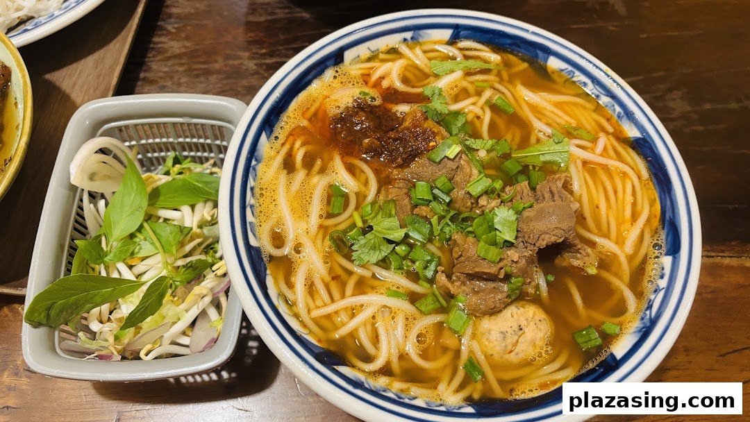 A vibrant bowl of Vietnamese noodle soup with beef, meatballs, and fresh herbs on a wooden table.
