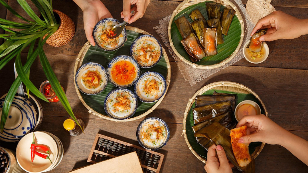 A top-down view of a wooden table laden with various authentic Vietnamese dishes, with hands enjoying the meal.