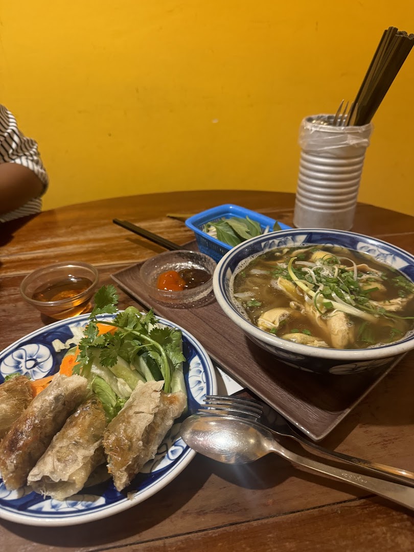 A table set with authentic Vietnamese spring rolls, a bowl of pho, and fresh herbs.