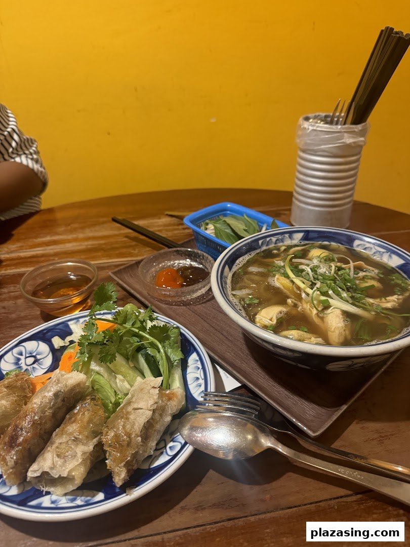 A table set with authentic Vietnamese spring rolls, a bowl of pho, and fresh herbs.