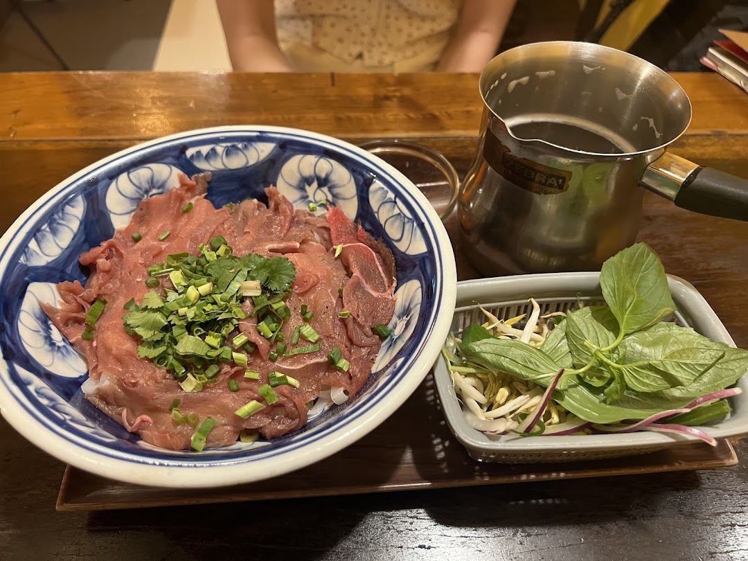 A bowl of Vietnamese pho with thinly sliced beef, fresh herbs, and a side of bean sprouts and basil.