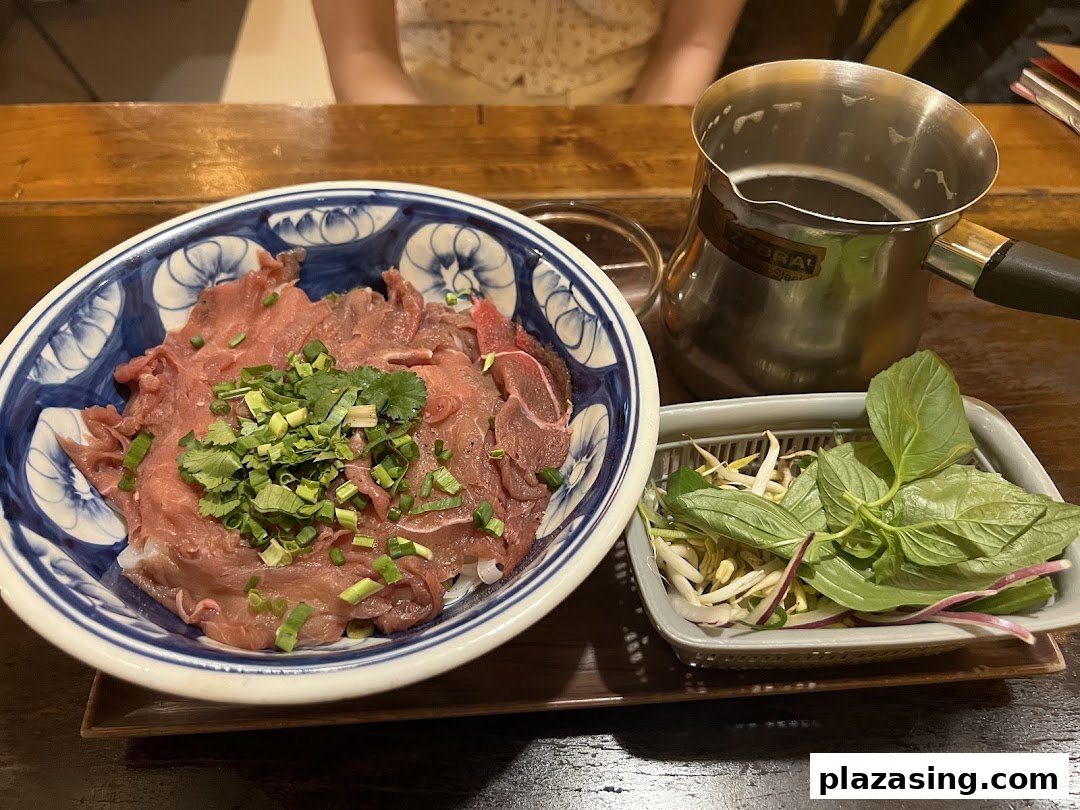 A bowl of Vietnamese pho with thinly sliced beef, fresh herbs, and a side of bean sprouts and basil.
