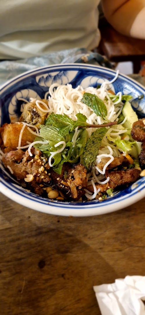 A vibrant bowl of Vietnamese vermicelli noodles with grilled meat, spring rolls, and fresh herbs.