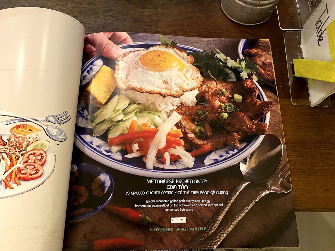 A close-up of a menu page featuring a Vietnamese broken rice dish with grilled pork and egg.