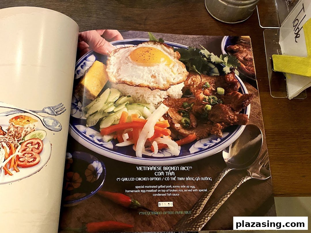 A close-up of a menu page featuring a Vietnamese broken rice dish with grilled pork and egg.