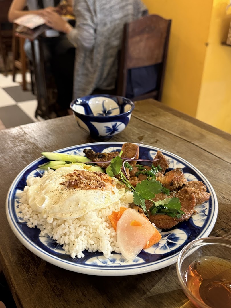 A vibrant plate of Vietnamese grilled pork with rice, fried egg, and pickled vegetables on a wooden table.