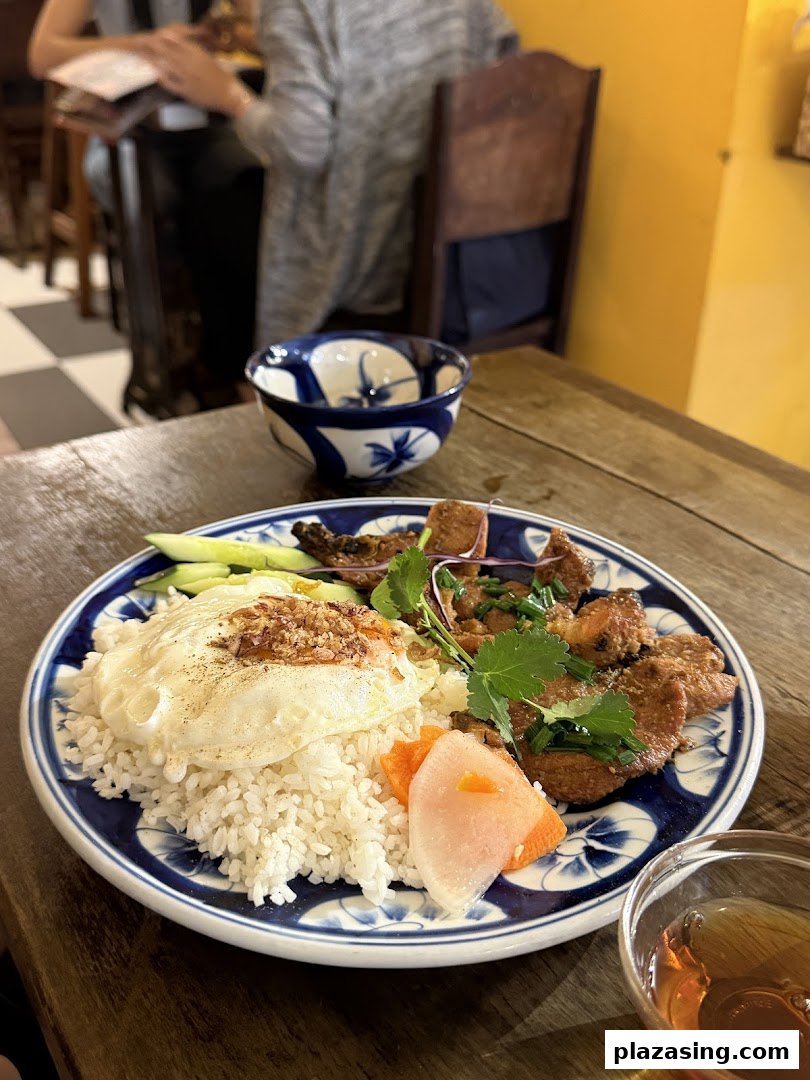 A vibrant plate of Vietnamese grilled pork with rice, fried egg, and pickled vegetables on a wooden table.
