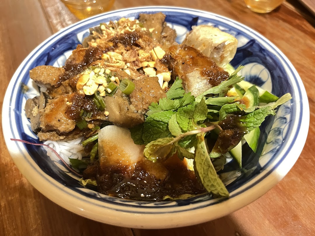 A vibrant bowl of Vietnamese noodles with grilled meat, fresh herbs, and a savory sauce.