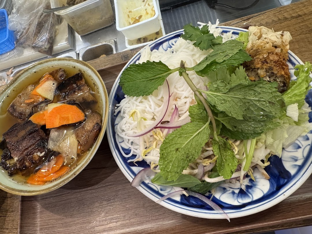 A vibrant Vietnamese dish featuring noodles, fresh herbs, and a spring roll, alongside a rich stew.