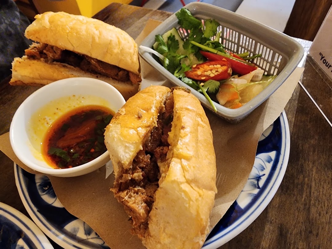 Two delicious Banh Mi sandwiches served with a side of fresh herbs, chili, and a flavorful dipping sauce.