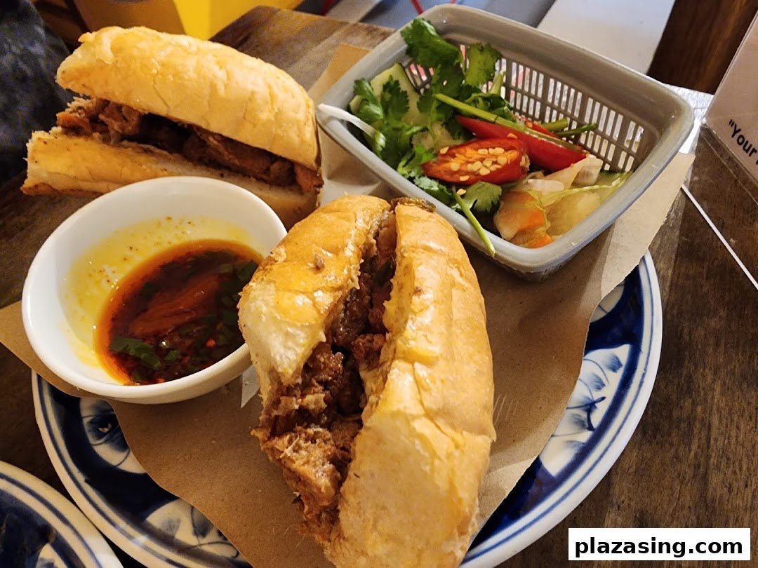 Two delicious Banh Mi sandwiches served with a side of fresh herbs, chili, and a flavorful dipping sauce.