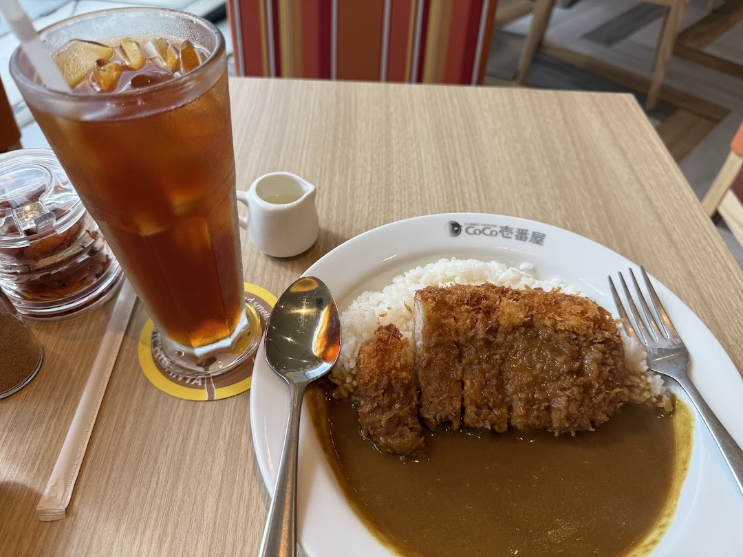 A plate of katsu curry with rice and a glass of iced tea on a wooden table.