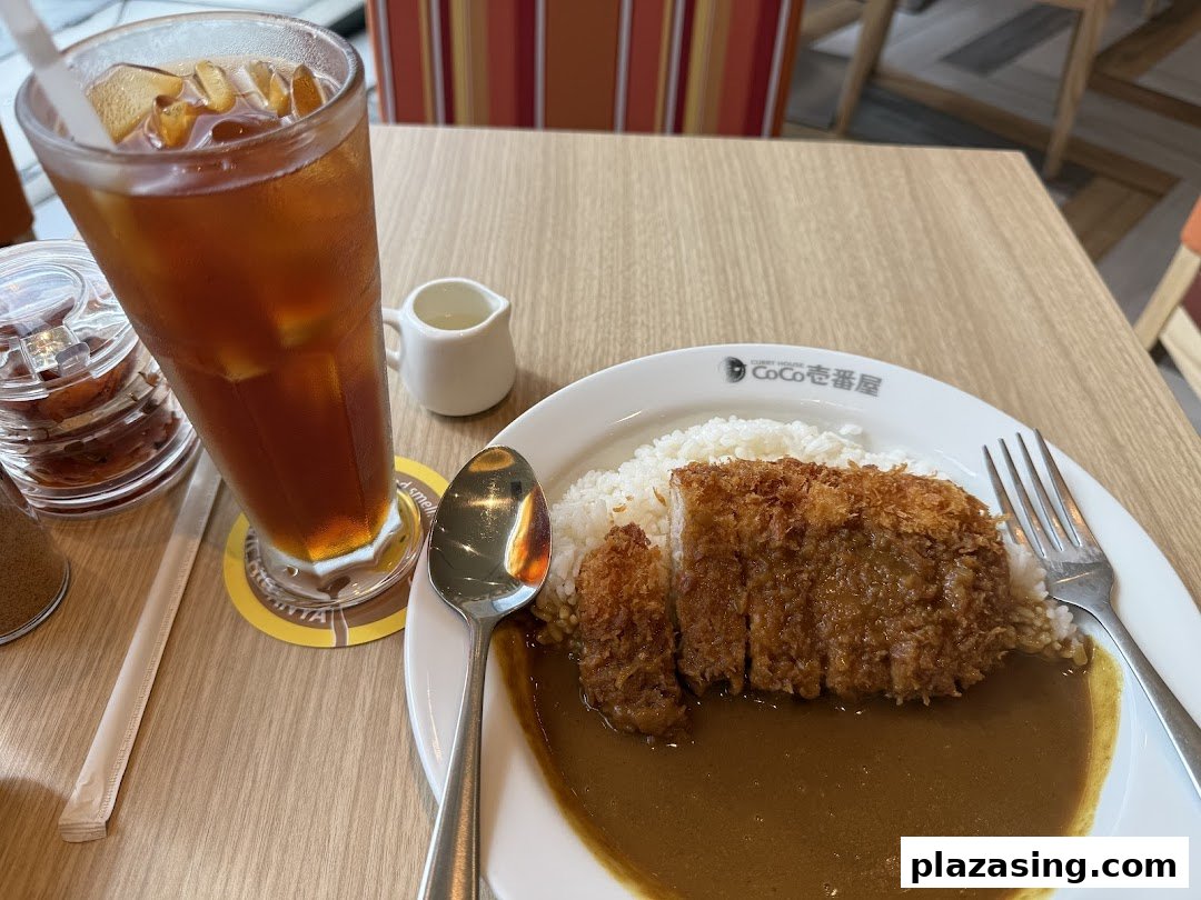 A plate of katsu curry with rice and a glass of iced tea on a wooden table.