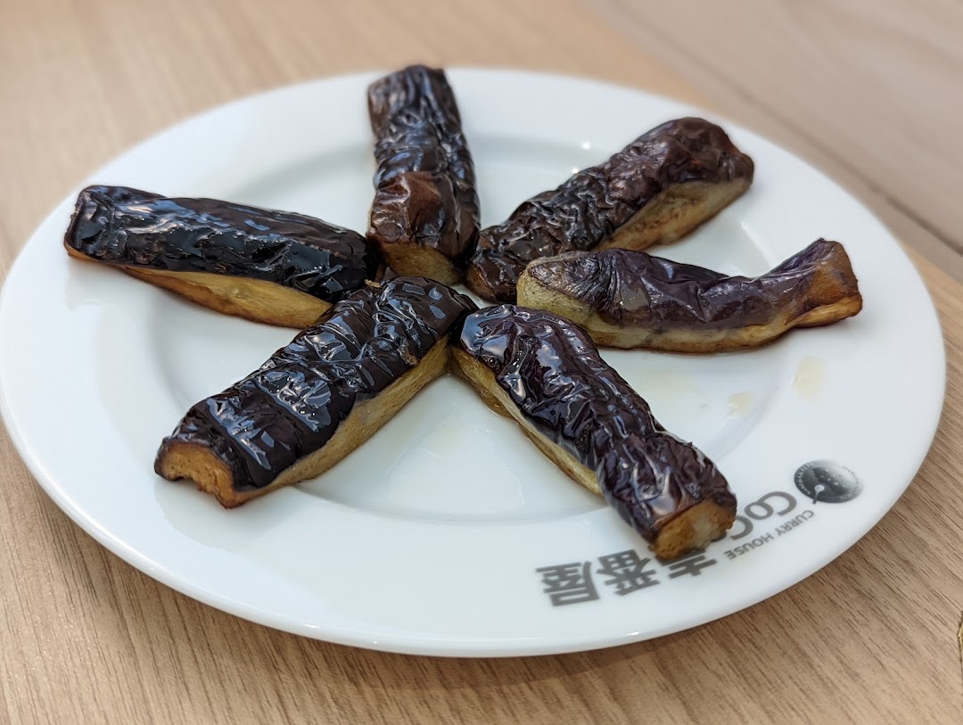 Six pieces of cooked eggplant arranged on a white plate with the CoCo ICHIBANYA logo.