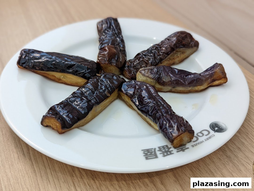 Six pieces of cooked eggplant arranged on a white plate with the CoCo ICHIBANYA logo.