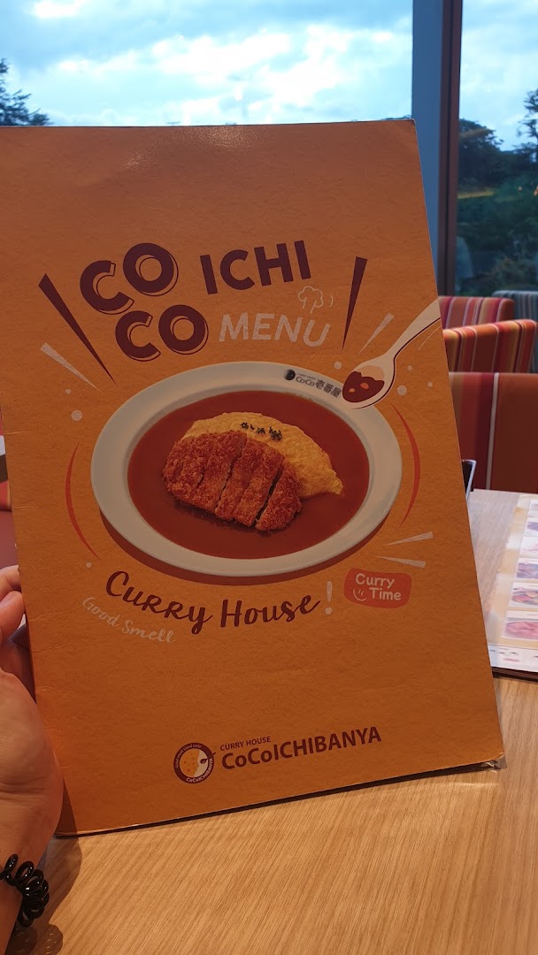 A hand holding the cover of a CoCo ICHIBANYA menu featuring a curry dish.