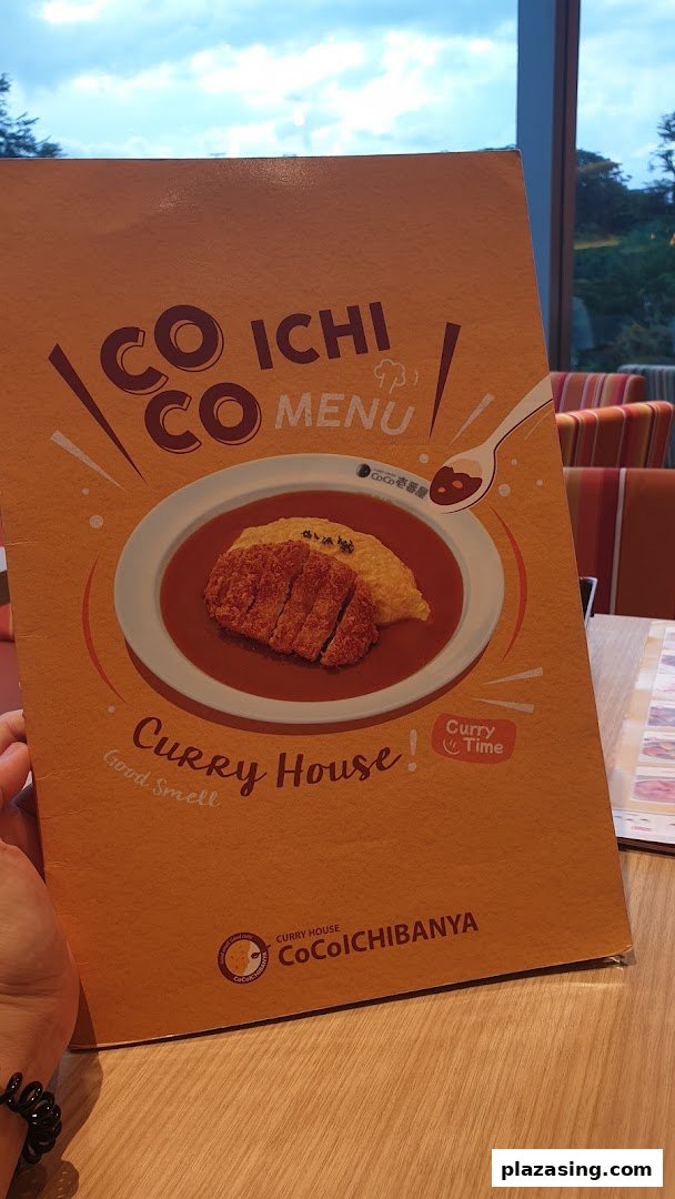 A hand holding the cover of a CoCo ICHIBANYA menu featuring a curry dish.