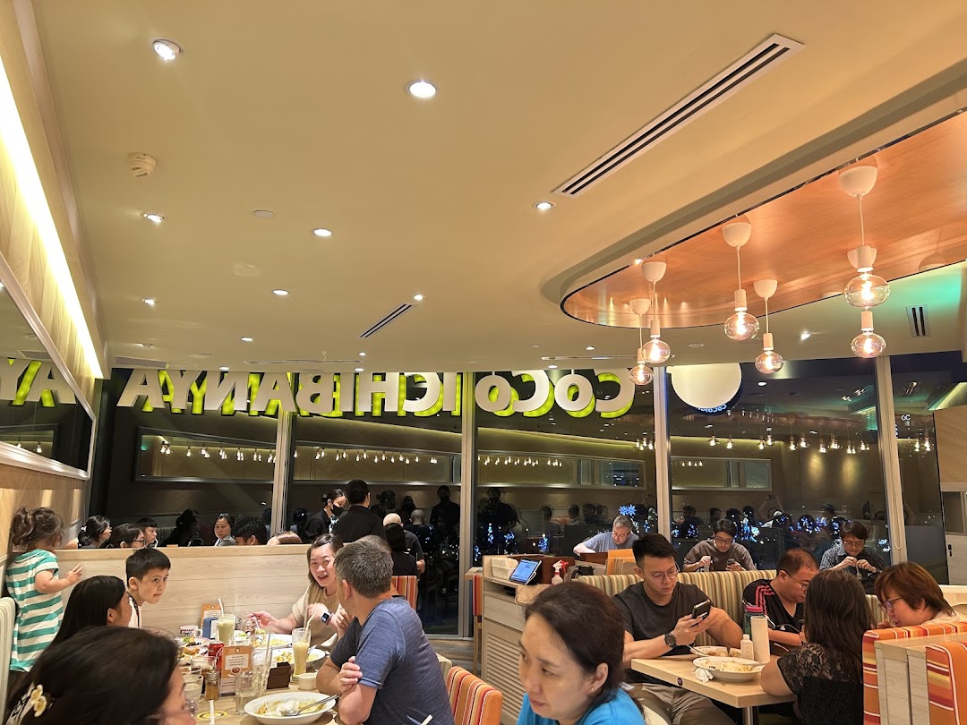Diners enjoy meals inside CoCo ICHIBANYA, with the restaurant's name reflected on the window.