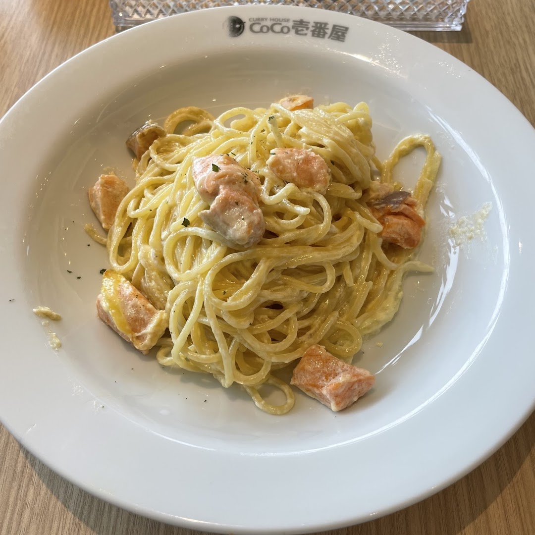 A close-up of creamy spaghetti with salmon pieces served on a white plate.