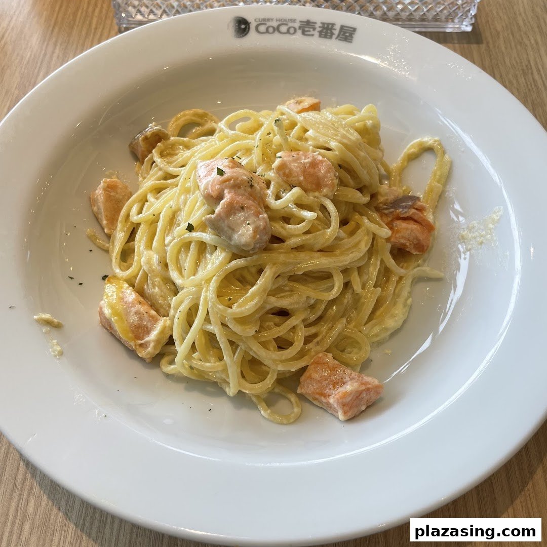 A close-up of creamy spaghetti with salmon pieces served on a white plate.