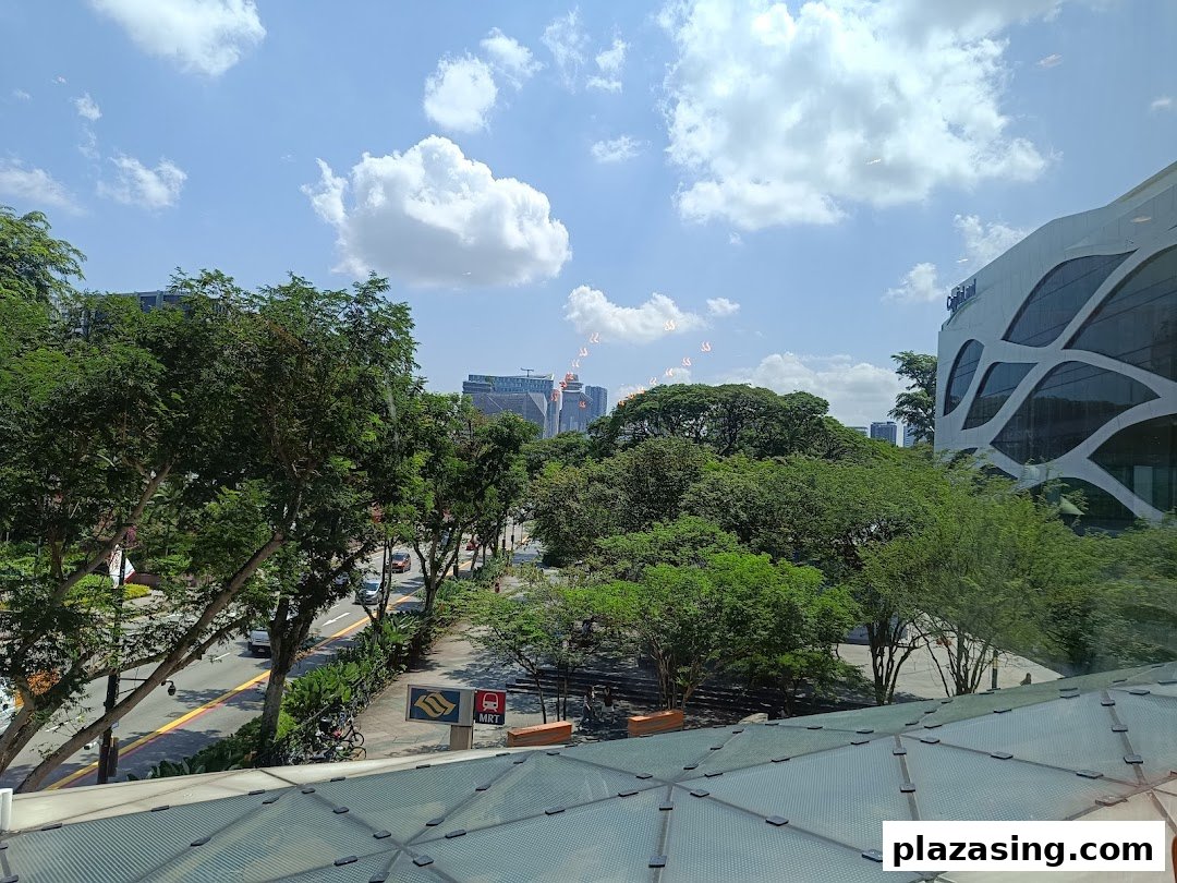 A bright outdoor view of a city street with lush trees and distant buildings under a clear sky.