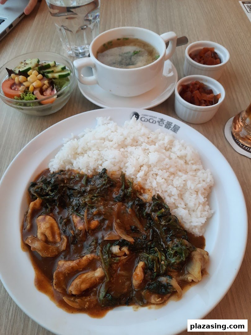 A delicious plate of Japanese curry rice with chicken, spinach, and onions, served with soup, salad, and pickles.