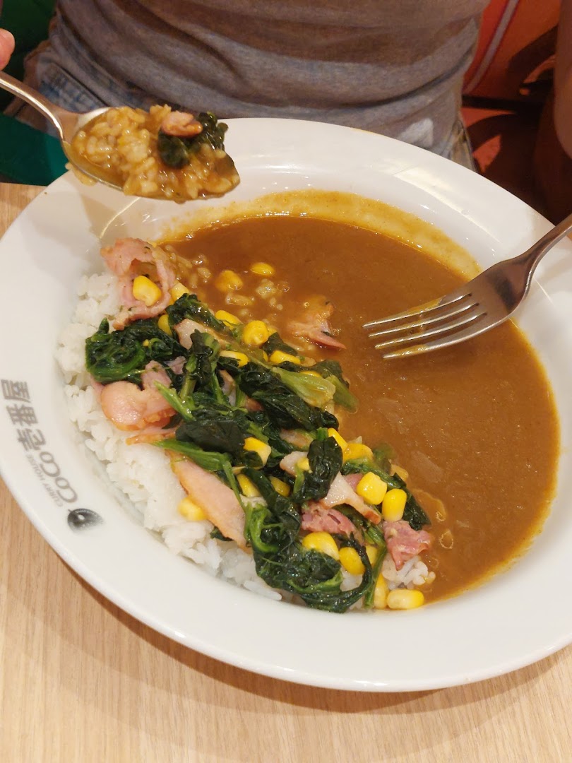 A delicious plate of CoCo ICHIBANYA curry rice with spinach, corn, and bacon toppings.