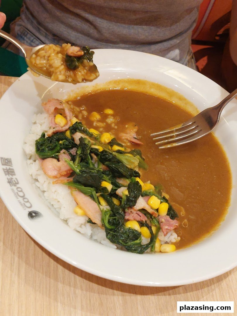 A delicious plate of CoCo ICHIBANYA curry rice with spinach, corn, and bacon toppings.