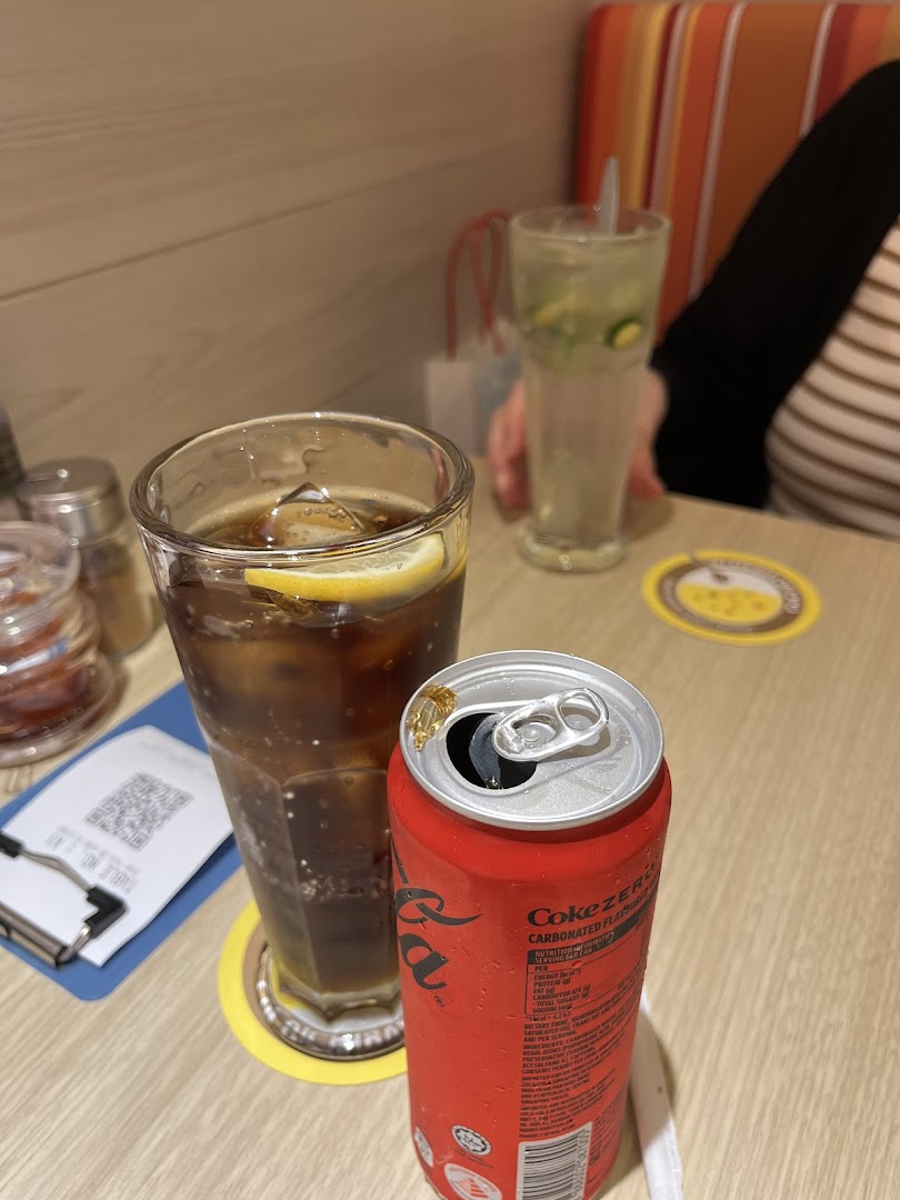 Two drinks, including a Coke Zero can and a cola with lemon, on a restaurant table.