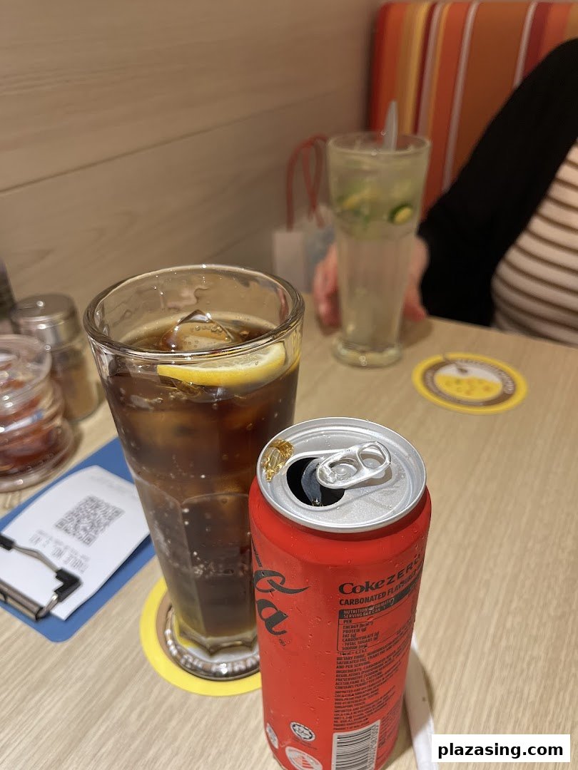 Two drinks, including a Coke Zero can and a cola with lemon, on a restaurant table.