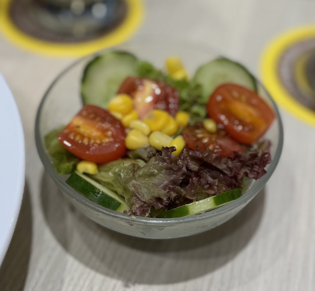 A fresh side salad with lettuce, tomatoes, corn, and cucumber in a clear bowl.