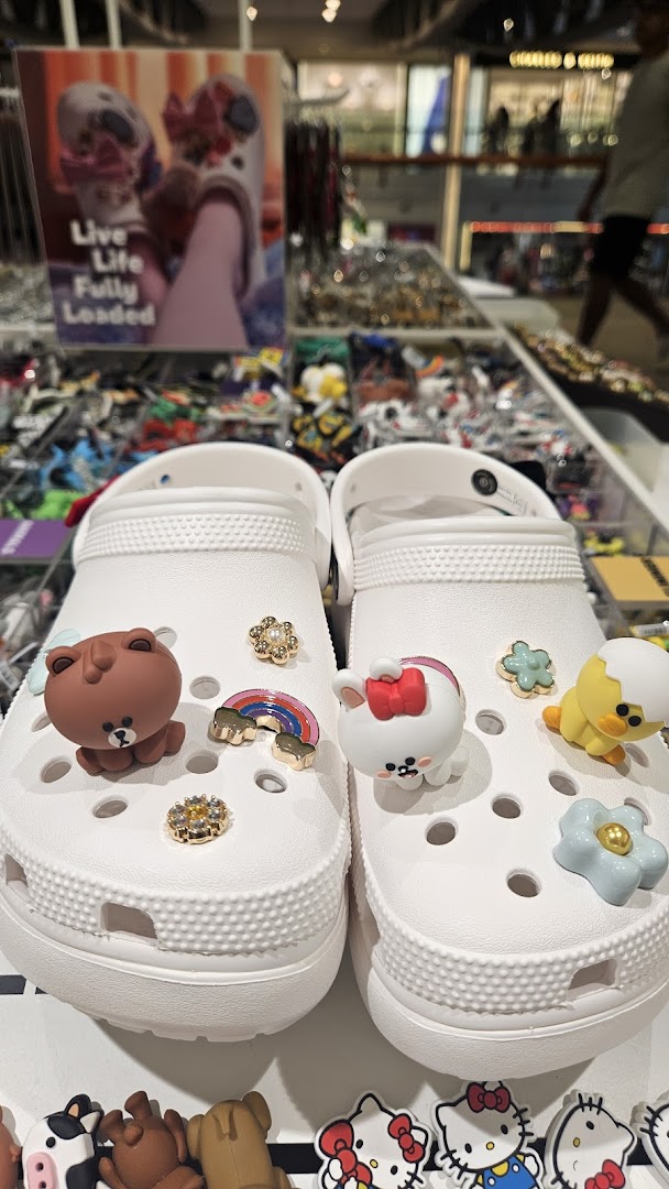 A pair of white Crocs adorned with various colorful and playful Jibbitz charms on display.