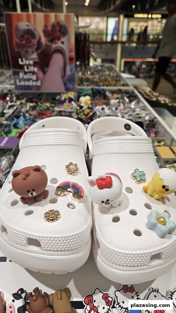 A pair of white Crocs adorned with various colorful and playful Jibbitz charms on display.