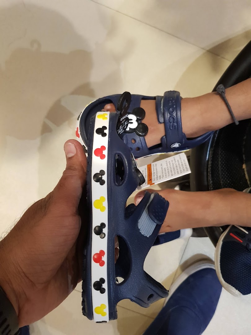 A hand holds a blue Crocs sandal with Mickey Mouse designs, next to a child's foot wearing a similar pair.