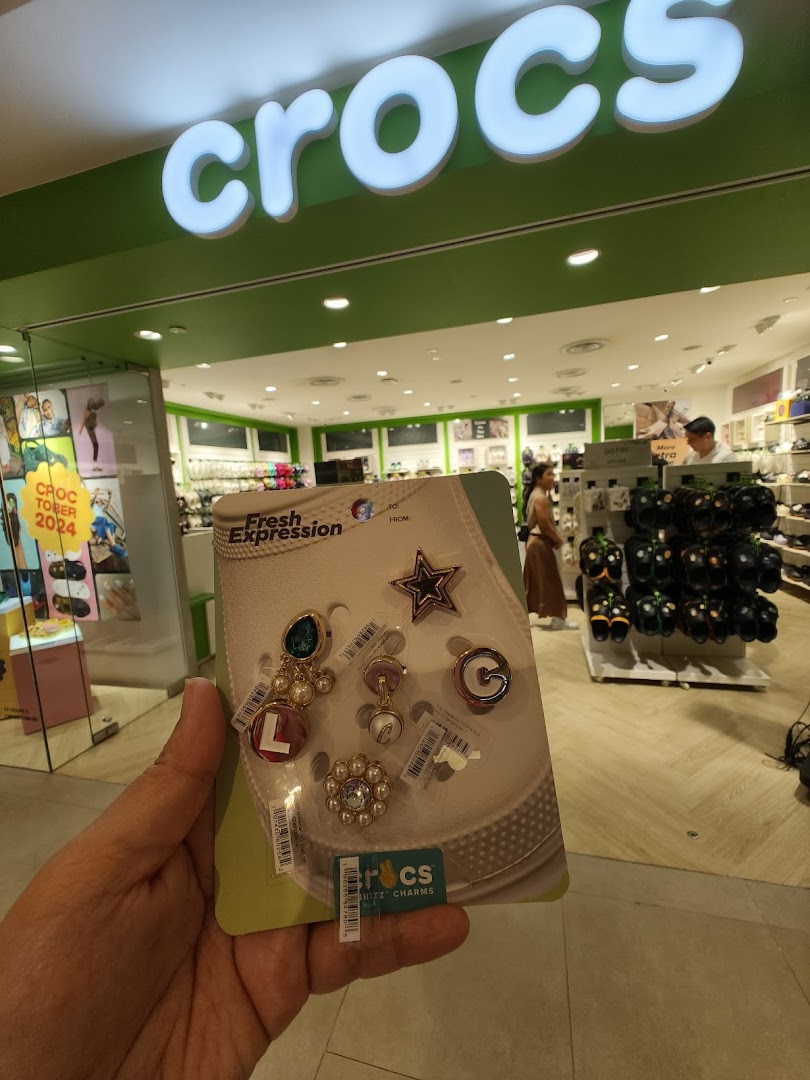 A hand holds Crocs Jibbitz charms inside a Crocs store, with the shop interior visible.