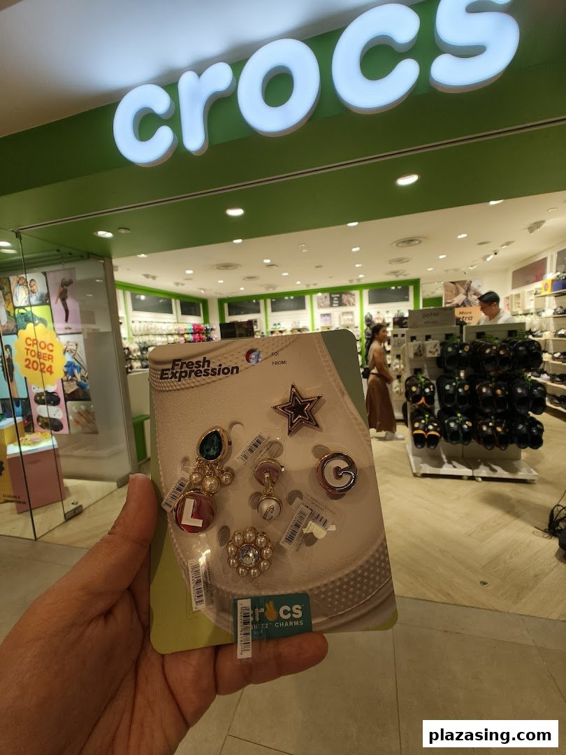 A hand holds Crocs Jibbitz charms inside a Crocs store, with the shop interior visible.
