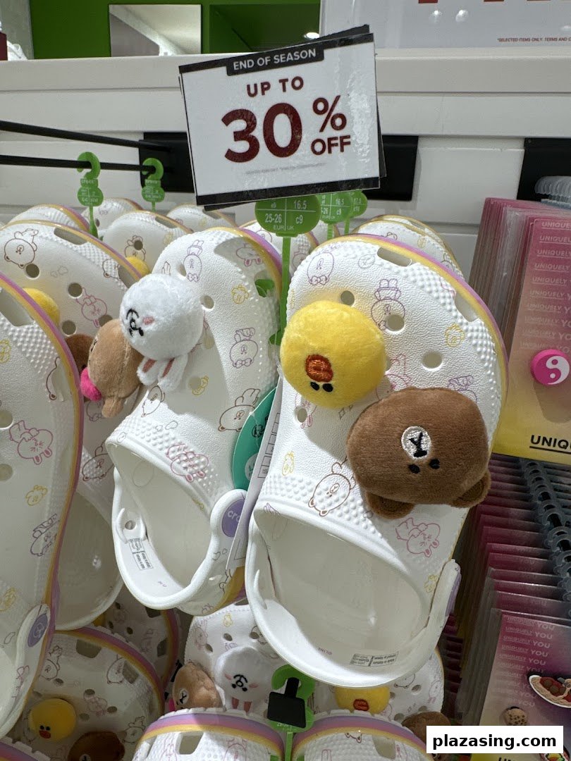 Close-up of white Crocs with character Jibbitz charms and an 'End of Season Up To 30% Off' sale sign.