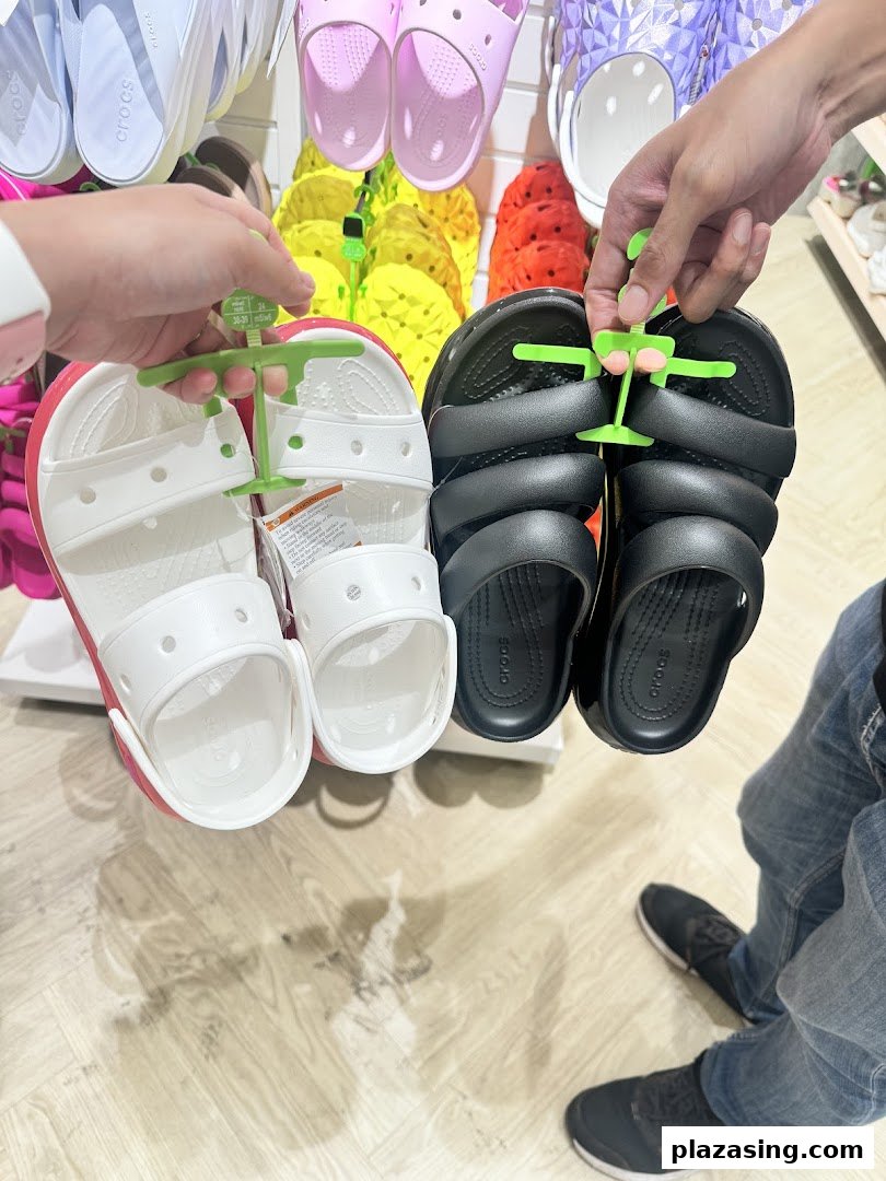 Two people hold up different styles of Crocs sandals in a vibrant store setting.